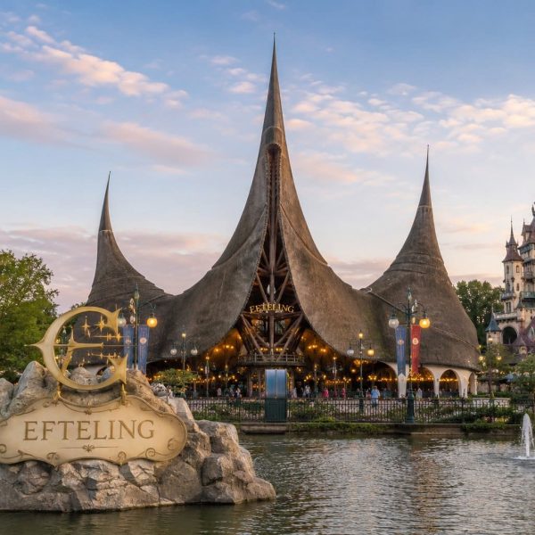 De iconische ingang van de Efteling tijdens zonsondergang met het sprookjesachtige entreegebouw, fontein en Efteling bord aan het water