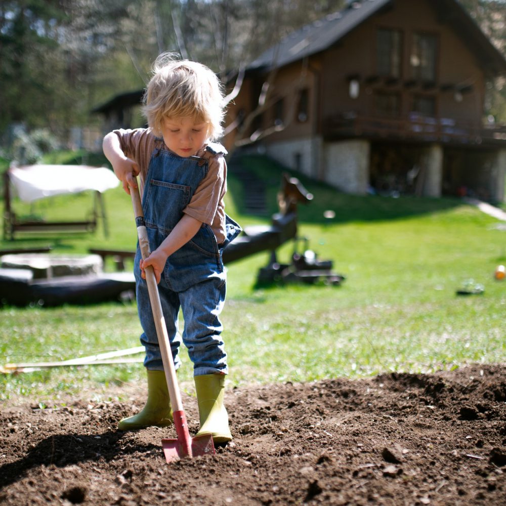 Small boy working outdoors in garden, sustainable lifestyle concept